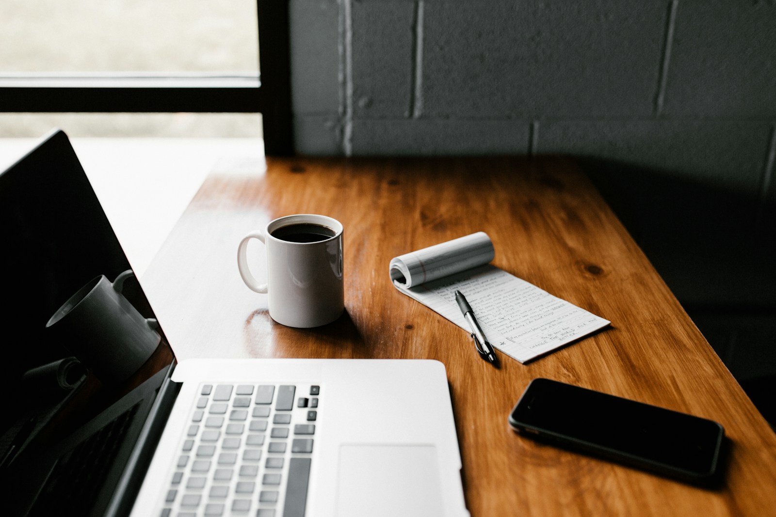 Editorial photograph of an inviting study desk with a laptop, notebook and coffee in soft natural light, warm neutral tones, no people